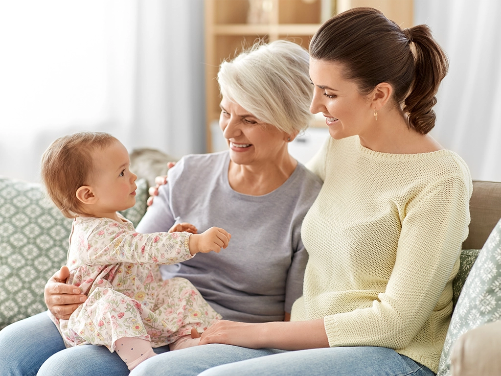 happy smiling mother baby daughter and grandmother sitting on sofa at home